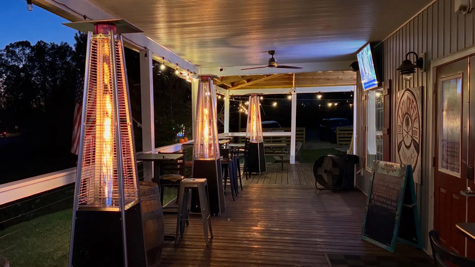 Covered porch at dusk with glowing patio heaters and string lights