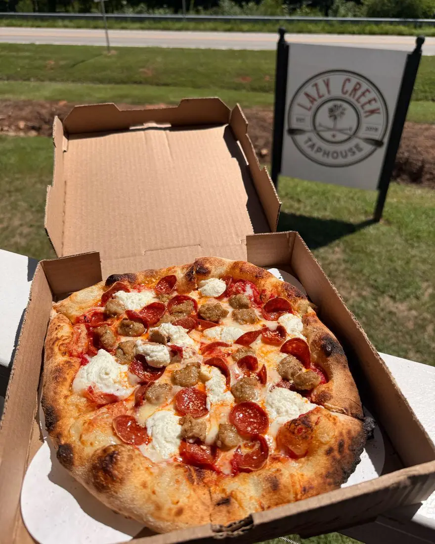 La Dolce Vita Pizza wood-fired pizza in an open box with the Lazy Creek Taphouse sign behind it